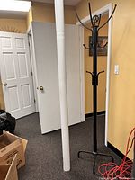 Photo of a black heavy duty coat stand with multiple hooks in an indoor setting near white walls and doors.