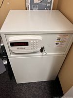 White rectangular Mesa electronic safe with front digital keypad, key lock, and operating instructions sticker.