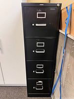 Front view of black metal filing cabinet with four drawers, top drawer locked.