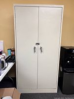 Front view of off-white metal storage cabinet with two doors closed, showing handles and lock latch.