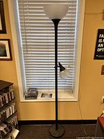 Standing black metal floor lamp with a white glass torchiere shade at the top and an adjustable reading lamp with a smaller white glass shade below.