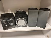 Photo showing the full stereo system: main unit, subwoofer, and two speakers on a shelf.