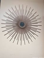 Photo of round metal sunburst wall art with long thin rods radiating from textured center.