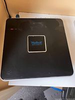 Top view of WinBook Security system main management unit, showing black casing with WinBook logo and indicator lights.