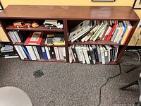 Two wooden bookcases filled with various binders, books, and some small collectibles such as model cars and other items. The shelves show medium brown wood with a few signs of wear.
