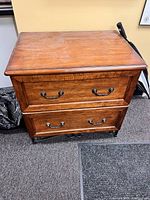 Wooden filing cabinet with two pull-out drawers, metal handles, and a medium brown finish. Measures about 2 feet wide, 3 feet high, and 2 feet deep as described by seller.