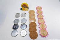 Array of four sets of coasters displayed on a white background: silver metal, cork, woven straw with pink edging, and citrus-themed stand.