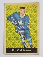 Front view showing Carl Brewer in Toronto Maple Leafs uniform against yellow background with Leafs logos and black nameplate.
