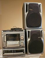 Overall stereo system stacked with two speakers on a table against a plain wall.