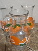Photo showing three clear glass pitchers with orange and green leaf design, placed together on a surface.
