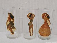 Three clear glasses with distinct dancing woman images on each, standing next to each other.