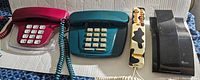 Lot of four vintage telephones displayed side by side on a flat surface showing overall condition and variety including rotary and push-button styles in multiple colors.