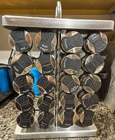 Front view of the spice rack showing 20 labeled spice jars including Basil, Black Pepper, Cinnamon, Cloves, Fennel, Garlic, Ginger, Mustard Seed, Oregano, Paprika, Parsley, Sage, Thyme and others.