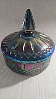 Side and angled view of carnival glass candy dish showing the lid, iridescence, and geometric pattern.