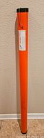 Full length image of the orange cylindrical Rod Caddy fishing rod case against a wall showing the full length and black cap.