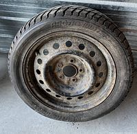 Single Arctic Winter 16 inch tire mounted on a rusty steel wheel, photographed against a corrugated metal background.