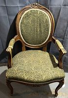 Front view of the antique Victorian arm chair showing carved wood frame and greenish-gold patterned fabric upholstery.