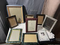Image showing 8 assorted picture frames arranged on a white cloth against dark and gray fabric background.