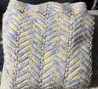 Folded crochet throw showing textured zigzag stitch pattern with pastel yarn in yellow, blue, pink tones.