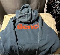Front view of blue Bench sweatshirt hoodie with large red 'Bench.' logo across chest and hood visible.