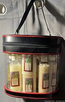 Clear plastic cylindrical traincase with black and red trim, containing bath accessories bottles and soap bars.
