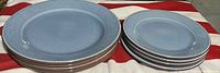 Photo showing 5 large and 5 smaller blue ceramic plates stacked on fabric surface.