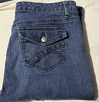 Jeans folded showing back pocket flap with silver button and dark blue denim fabric.