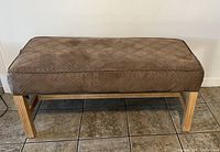 Photo of hallway bench showing the padded cushion seat with diamond pattern and light wood legs on tiled flooring.
