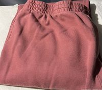 Folded dusty rose colored ladies sweatpants with elastic waistband shown in natural light.