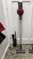 Full view of Dyson cordless stick vacuum with wand attached to motor unit, two floor heads, wall mount bracket, charger, crevice and brush attachments