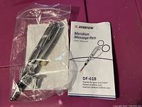 Meridian massage pen in sealed plastic packaging alongside its user manual titled 'Meridian Massage Pen DF-618'.