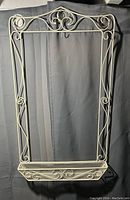 Front view of metal hanging calendar holder with scrollwork and mesh compartment, shown against dark background.