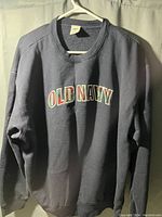 Photo of a gray Old Navy sweatshirt hanging on a hanger, showing the front logo and condition.