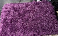 Close-up image of a deep purple fuzzy bathmat showing its texture and condition