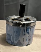 Front side view of push down smokeless ashtray showing currency note decoration and metal top with push knob