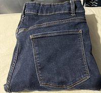 Folded dark blue jeans showing back pocket and stitch details.