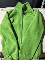 Green fleece sweater laid flat, showing full front zipper and collar with embroidered Columbia logo on the chest.