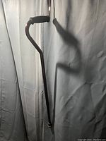 Photo of the walking cane showing the full length with a dark wooden shaft, curved handle with foam grip, and black rubber tip at the base.