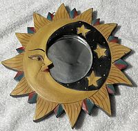 Photo of a wooden wall hanging mirror showing a crescent moon with stars on a sunny background with painted features.
