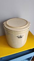 Full view of antique stoneware crock with lid on top of yellow surface.