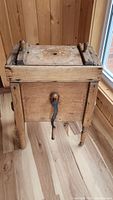 Front view showing wooden churn box with attached iron hand crank and turned legs