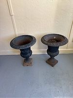Front view of two cast iron urn planters side by side on floor against wall
