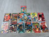 Top-down photo of all 13 comic books laid flat showing covers of iconic superheroes The Flash, Spider-Man, Justice League, Batman, Superman.