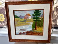 Framed oil painting showing entire artwork with house, river, trees, and mountains under a muted sky, featuring a wooden frame and beige mat.