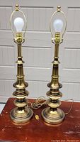 Pair of mid-century modern style solid brass Stiffel lamps with bulb and harp but no shades, sitting on wood surface.