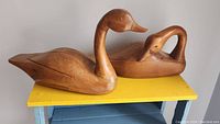 Pair of wooden goose decoys displayed on a yellow wooden stand, showing their size and positioning.