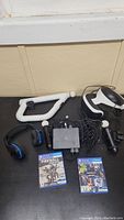 PlayStation VR headset, two PlayStation Move controllers, two remotes, headphones, VR toy gun accessory, connection cables, and two PS4 VR games on a black surface.