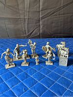 Photo showing nine pewter figurines arranged on blue quilted fabric, including dancers, musicians, and animal figures.