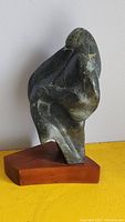 Front angled view of abstract soapstone carving on wooden base showing smooth flowing contours and natural variegated stone color.