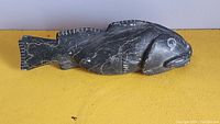 Side view of carved black soapstone fish sculpture with visible natural veining and carved fin details.
